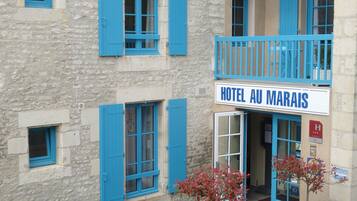 Et hotel med et skilt, der siger "HOTEL AU MARAIS". Det har stenvægge, blå skodder og en balkon med gelænder.