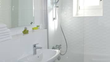Un baño moderno con ducha de vidrio, lavamanos blanco y un espejo grande.