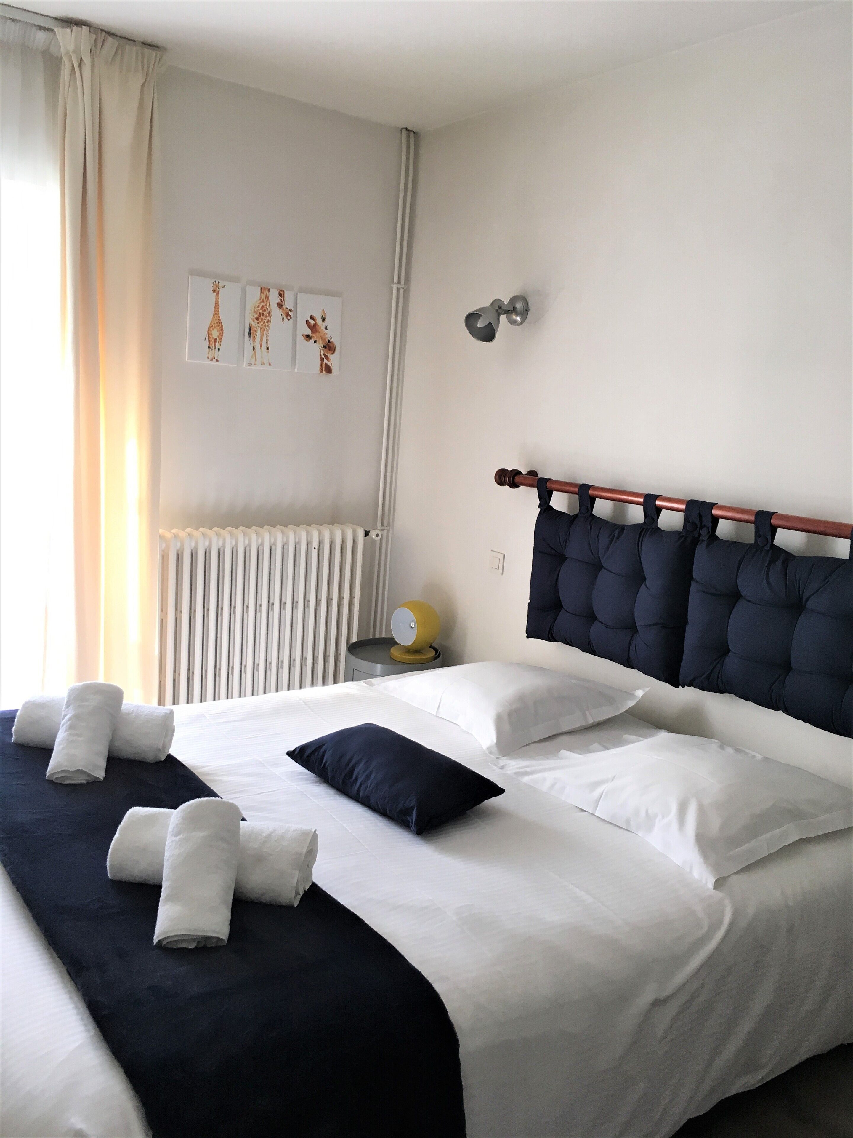 Un lit bien fait, avec une literie blanche et bleu marine, une tête de lit avec un cadre en bois, une lampe de chevet et un radiateur.