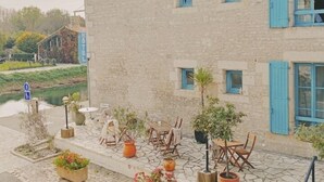 Un edificio con contraventanas azules y un patio empedrado con muebles de exterior y plantas en macetas.