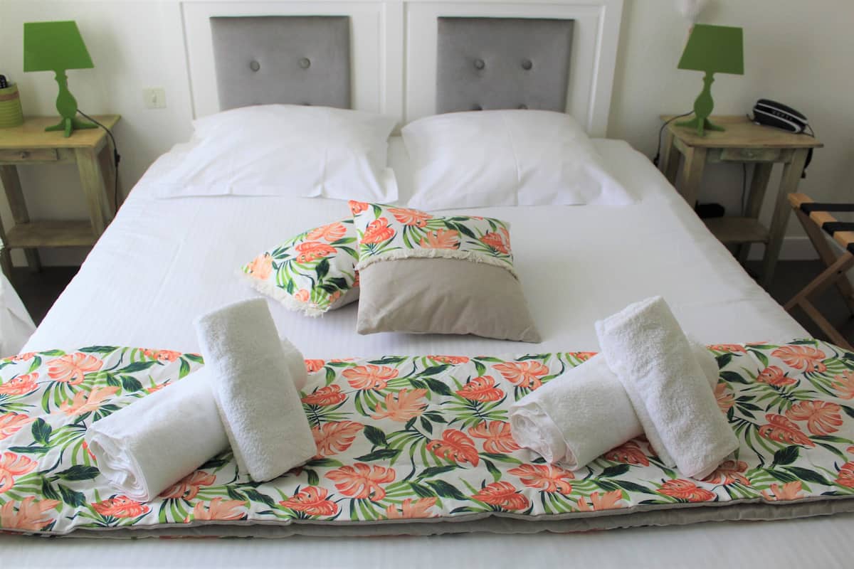 Una cama bien hecha con ropa de cama floral, dos almohadas y dos toallas enrolladas. Hay dos mesitas de noche, con lámparas y un teléfono sobre una de ellas.