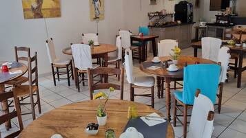 A dining area with round wooden tables, chairs, and a kitchen area in the background.