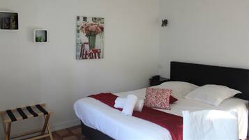 A neatly made bed with white linens and a red blanket, a small bedside table with a lamp, and a painting of flowers on the wall.