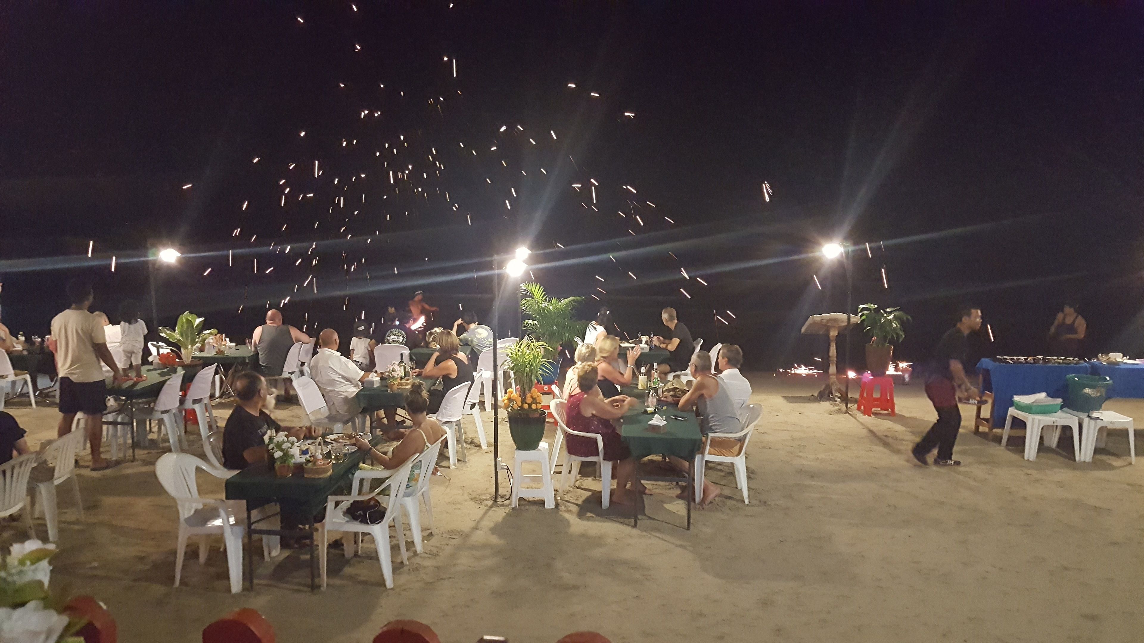 Un espacio de comedor al aire libre con mesas y sillas, rodeado por un entorno arenoso.
