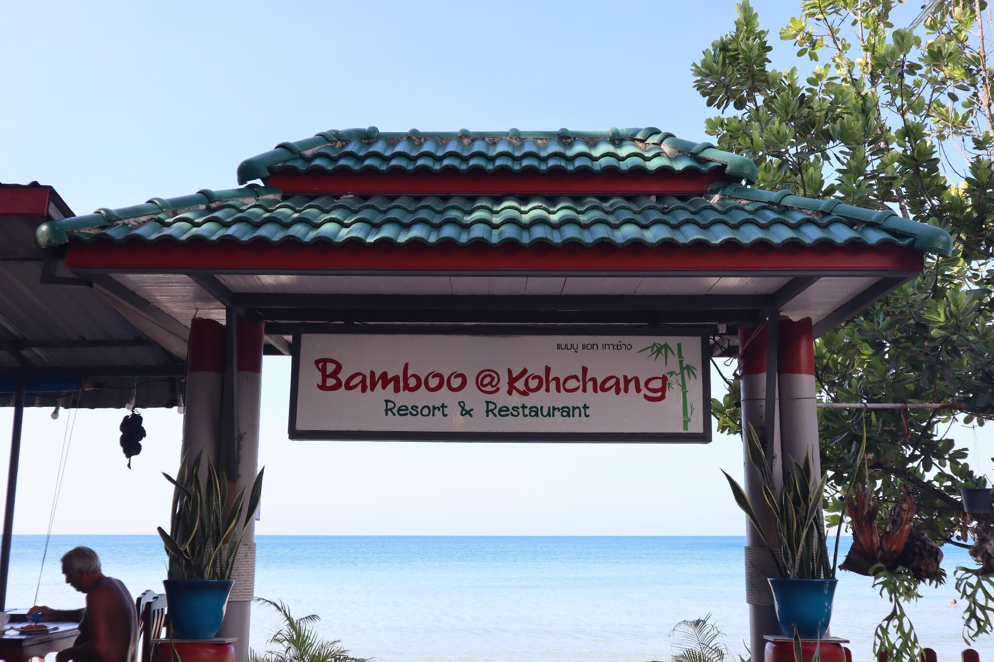 Schild eines Resorts und Restaurants mit Ziegeldach und Topfpflanzen.