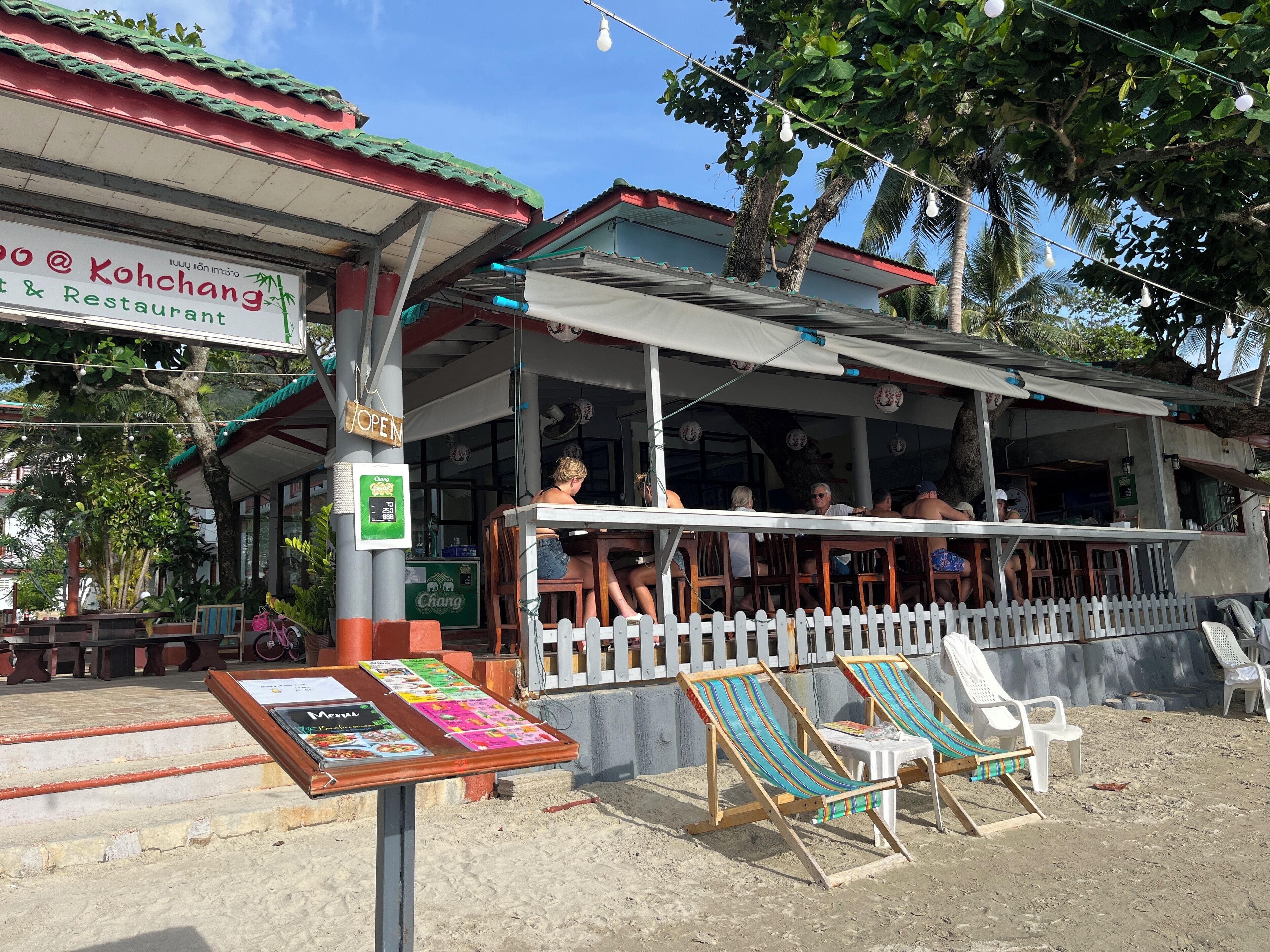A restaurant with outdoor seating, a signboard, and a menu display.