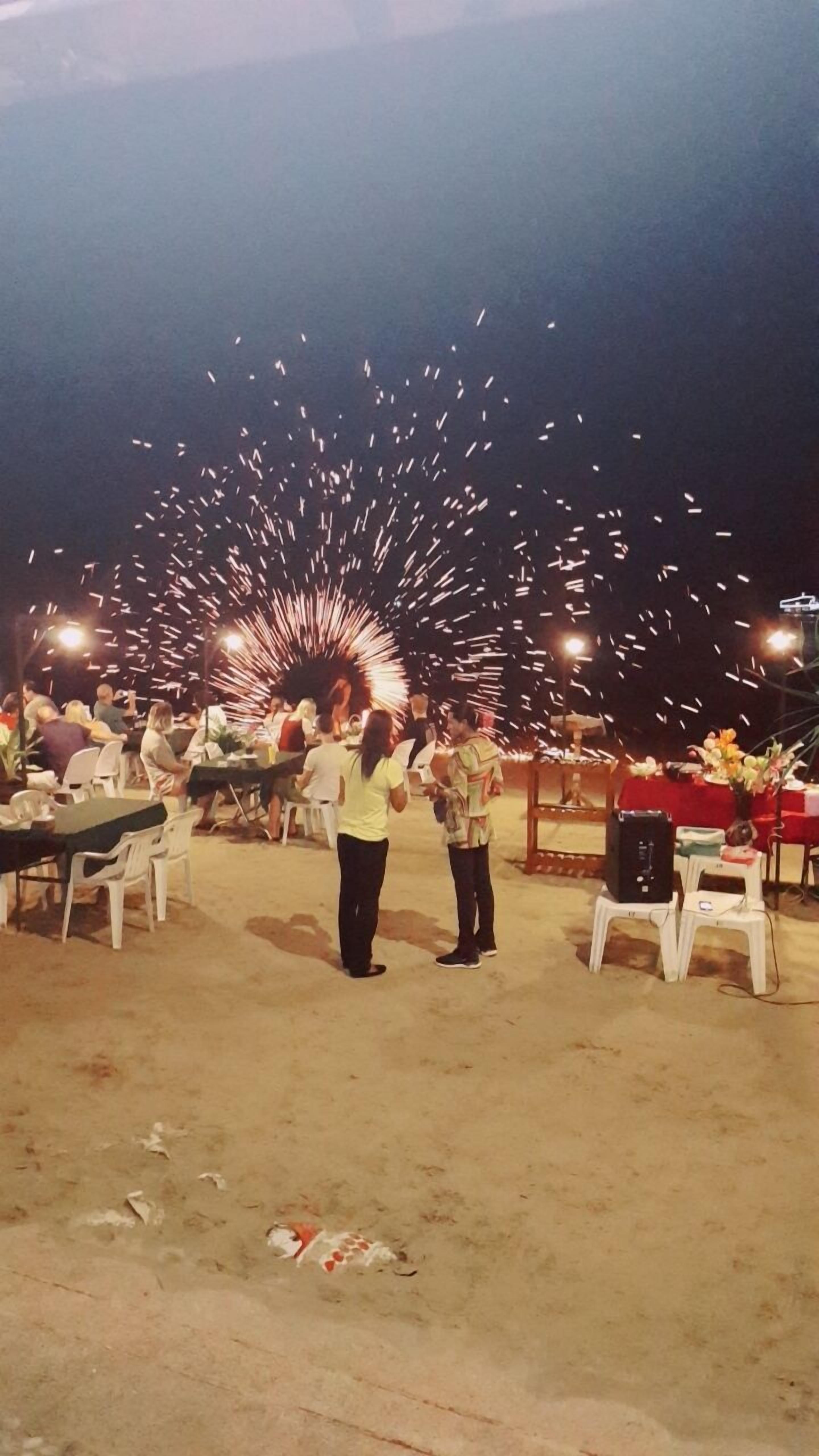 An outdoor event with tables and chairs arranged for guests, fireworks in the background, and a clear night sky.