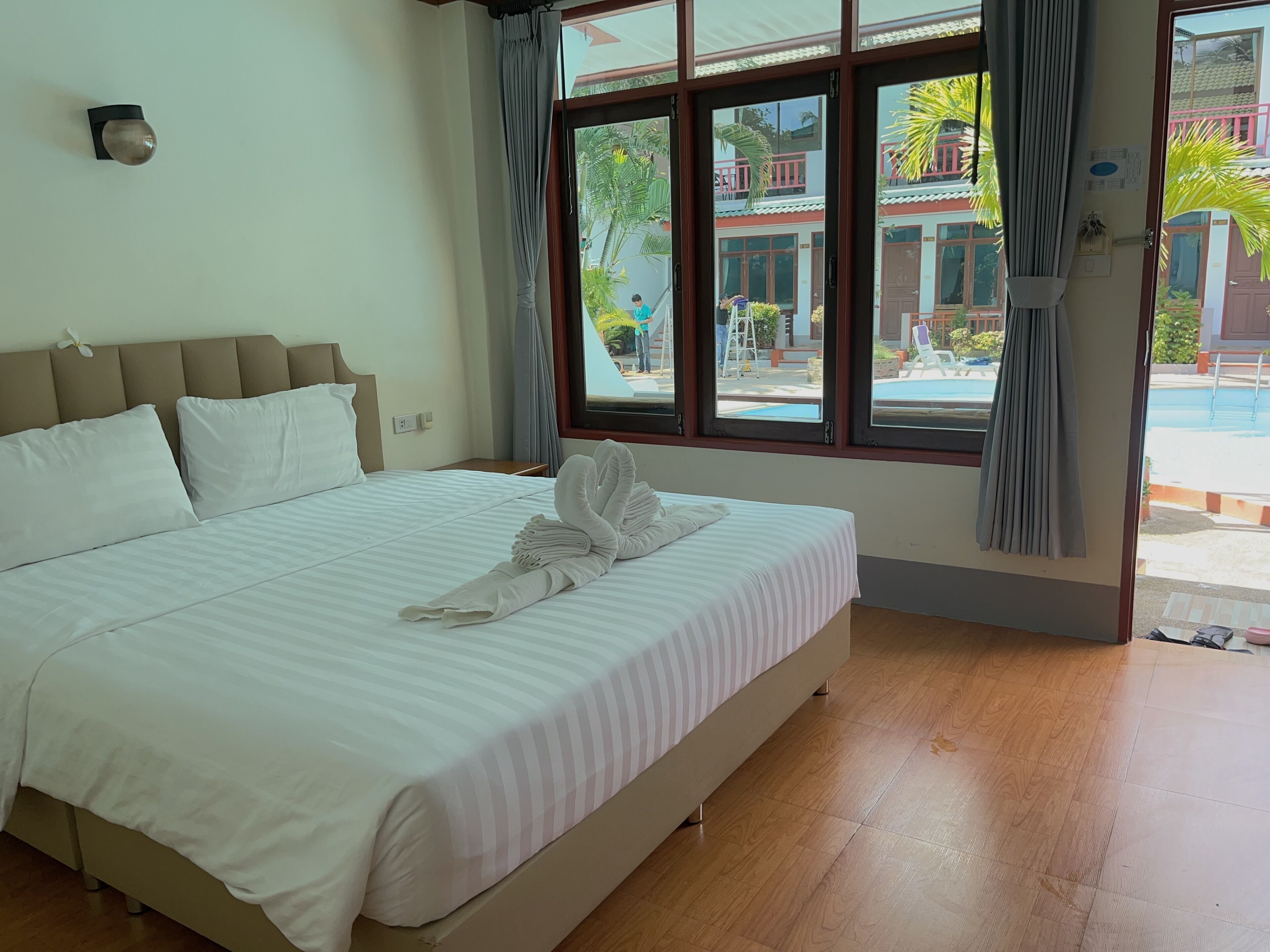 A hotel room with a large bed, a headboard, a window with curtains, and a view of the outside.