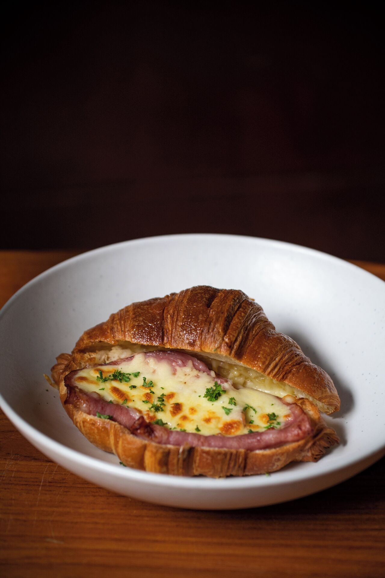 A croissant sandwich with cheese and ham on a white plate.