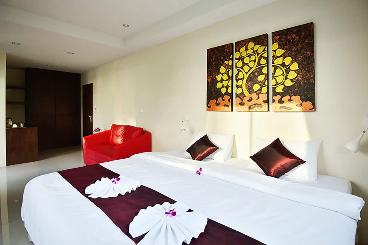 A hotel room with a large bed, a red armchair, and a painting on the wall.