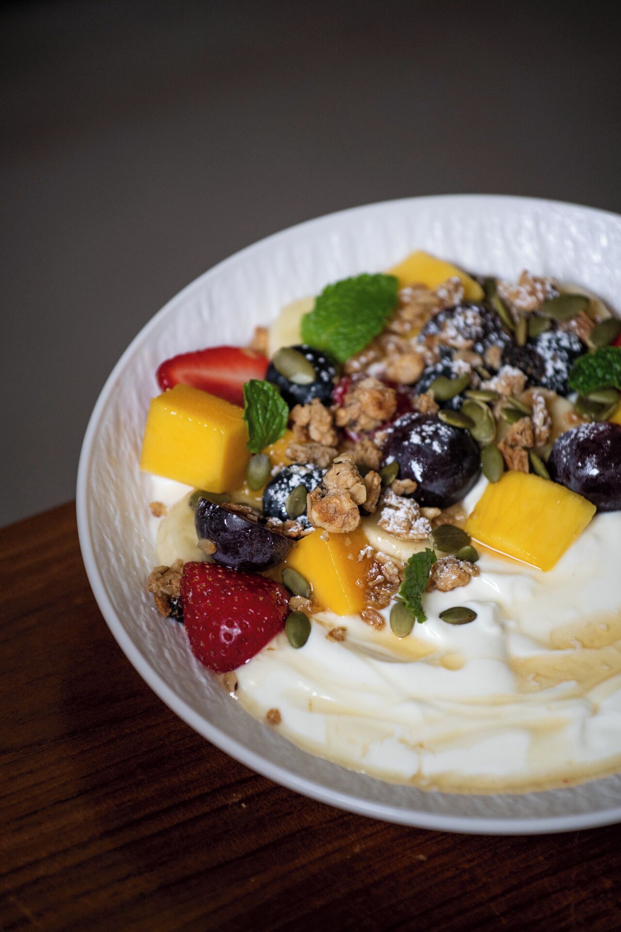 A bowl of yogurt topped with fruits, granola, and seeds.