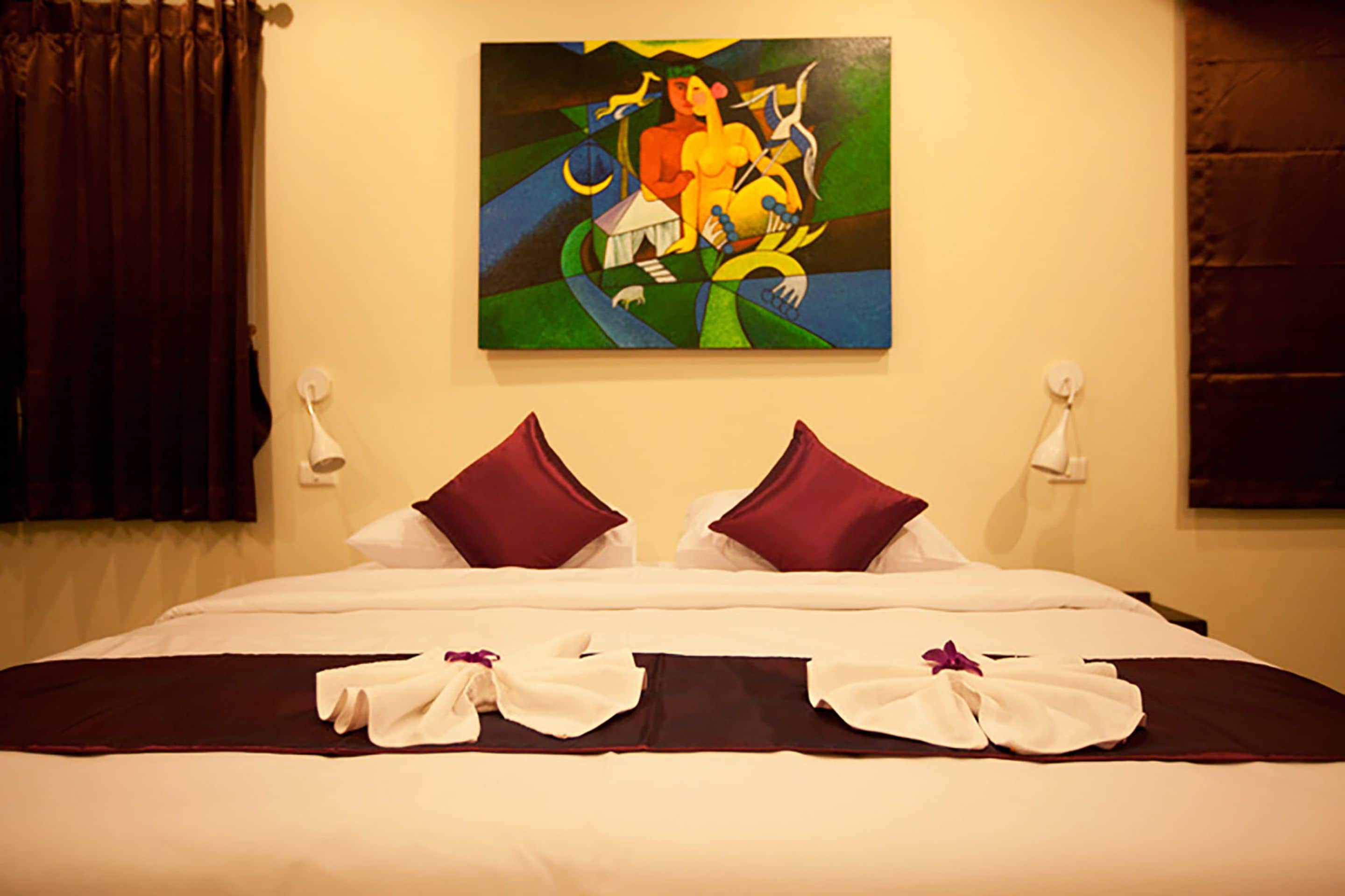 Una habitación de hotel con cama, almohadas, un cuadro en la pared y una ventana con cortinas.