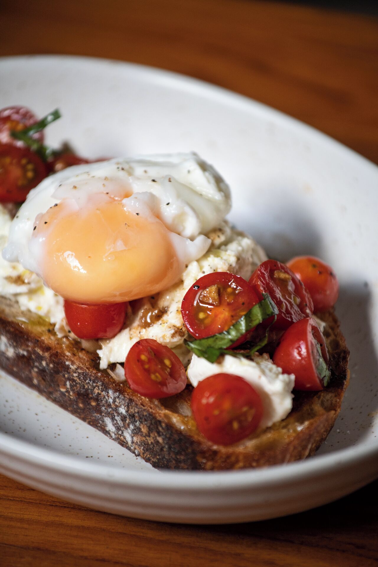 Une assiette avec une tranche de pain grillé garnie d’un œuf poché, de tomates cerises et de basilic.