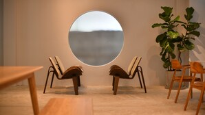 A room with a round mirror on the wall, two wooden chairs, a potted plant, and a wooden table. - At Kamala Hotel (Kamala)