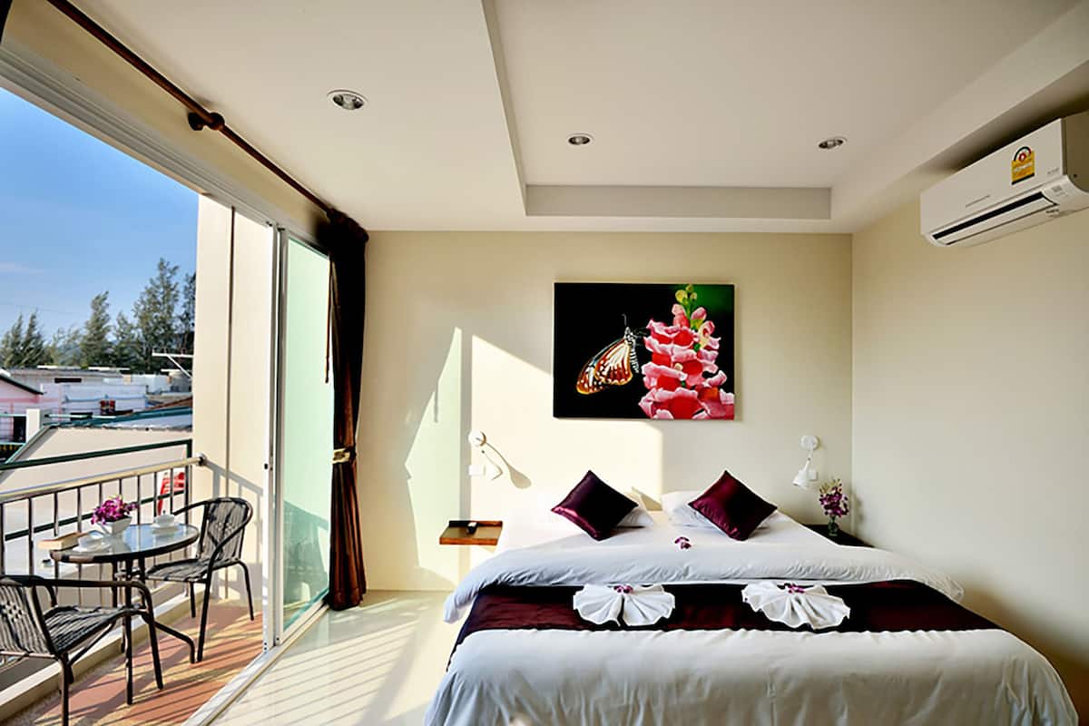 A hotel room with a balcony, a bed with white bedding, a painting of flowers, and a view of the outside.