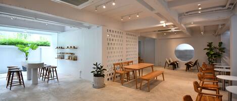 A modern interior with a central wooden table and benches, surrounded by white walls and a large window.