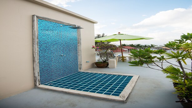 A covered outdoor shower area with a tiled floor, a potted plant, and a green umbrella. - At Kamala Hotel (Kamala)