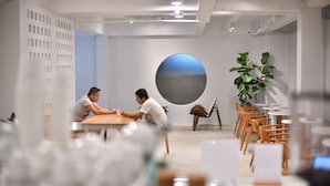 A modern meeting room with two people seated at a table, a large circular artwork on the wall, and several chairs and tables arranged around the room. - At Kamala Hotel (Kamala)