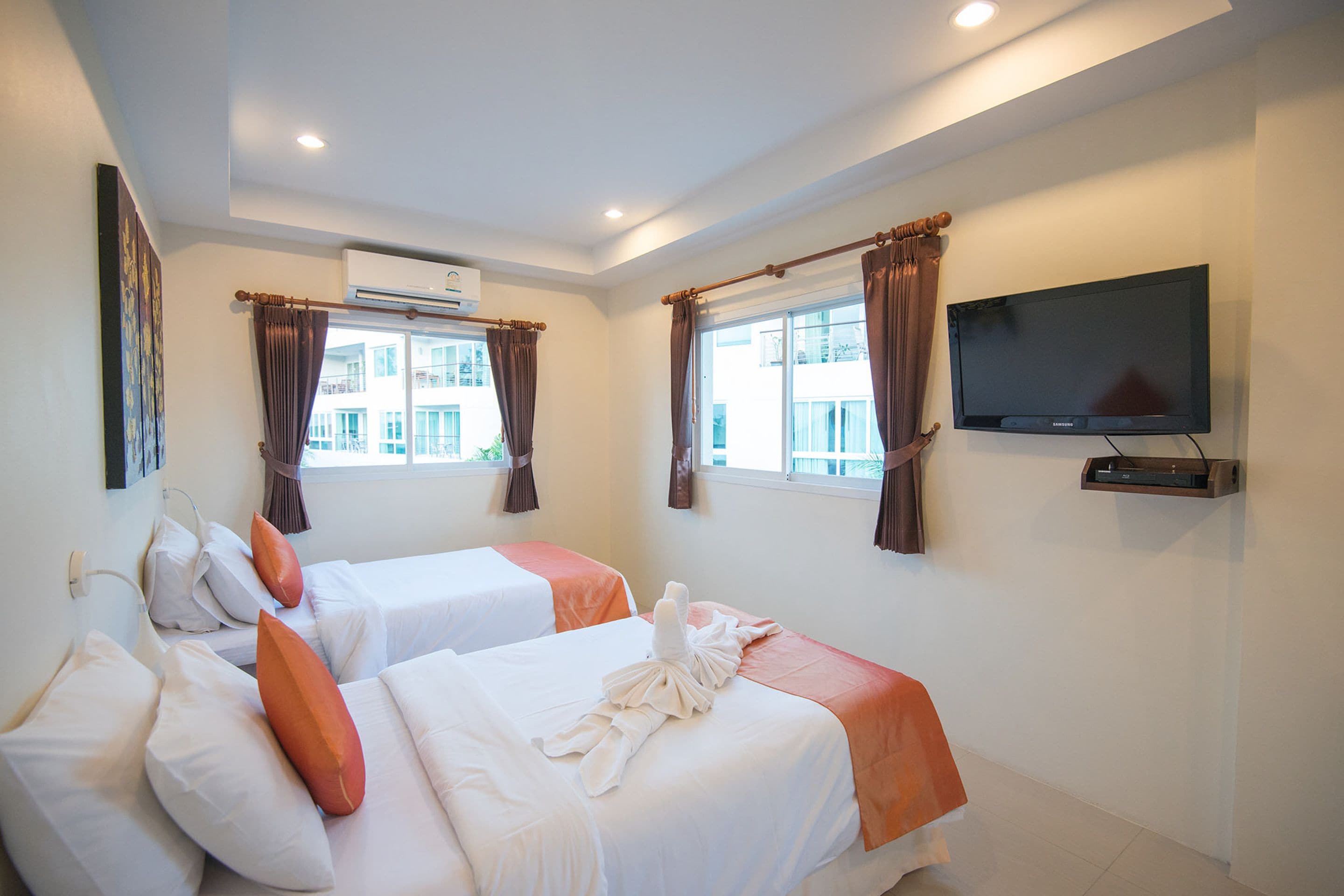 A hotel room with two beds, a flat-screen TV, and an air conditioning unit.