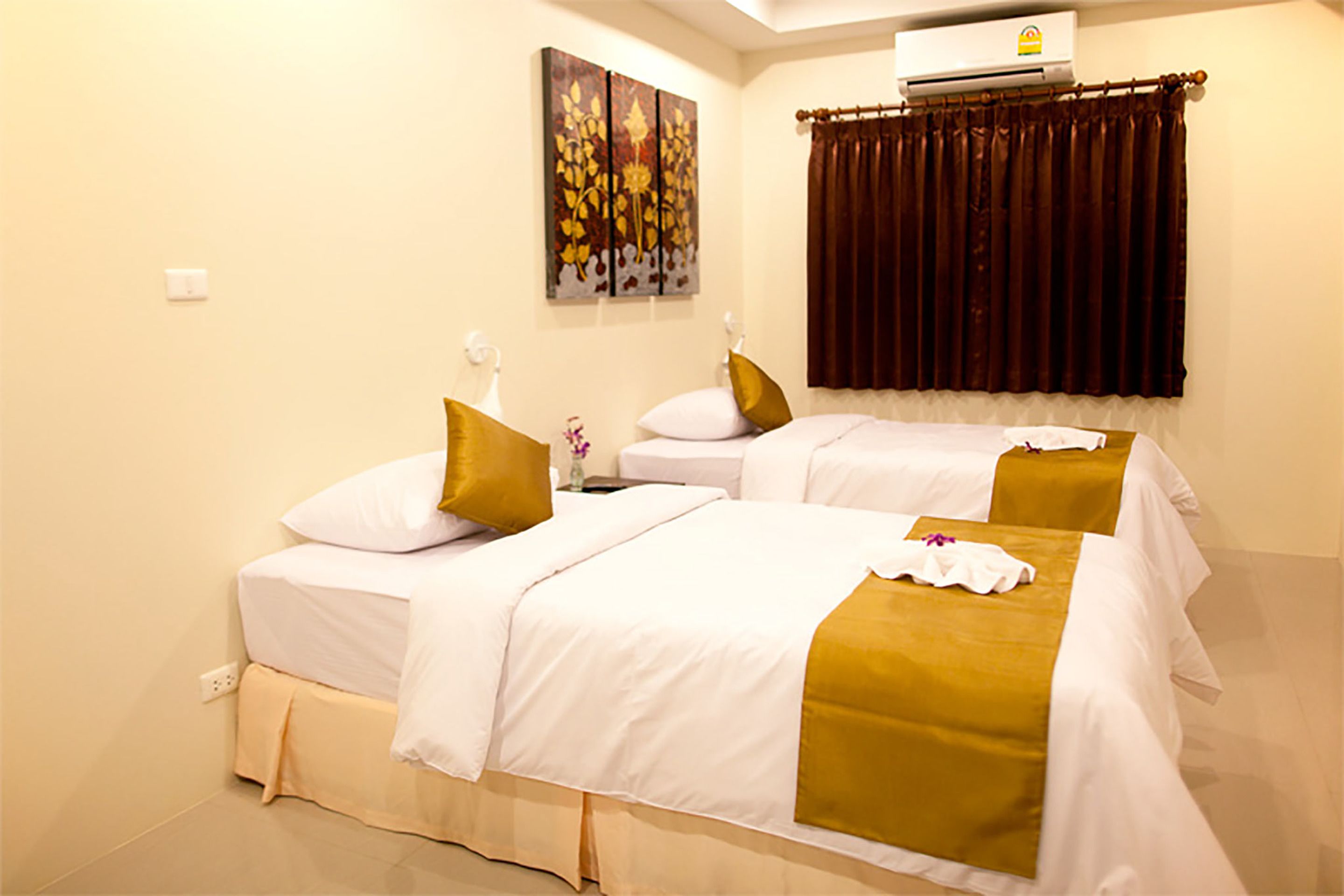 A hotel room with two beds, each with white bedding and gold accents, a painting on the wall, and an air conditioning unit above the beds.
