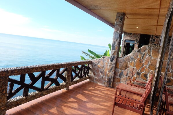 Un balcón con pared de piedra, barandilla de madera y vista al mar.