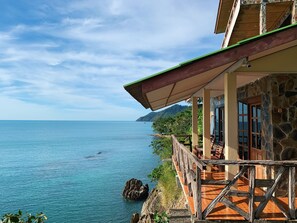 Un edificio costero con fachada de piedra, terraza de madera y vistas al mar.