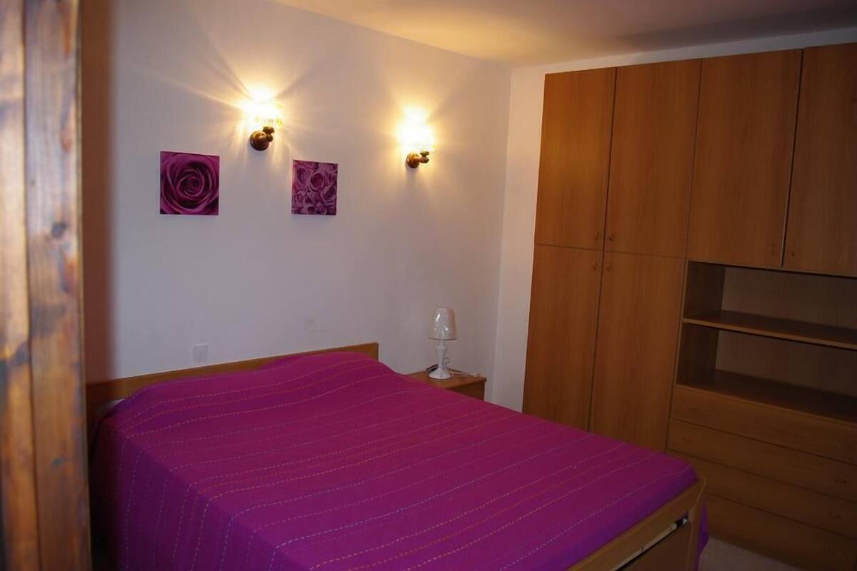 A bedroom with a bed, wooden wardrobe, and two wall-mounted lights.