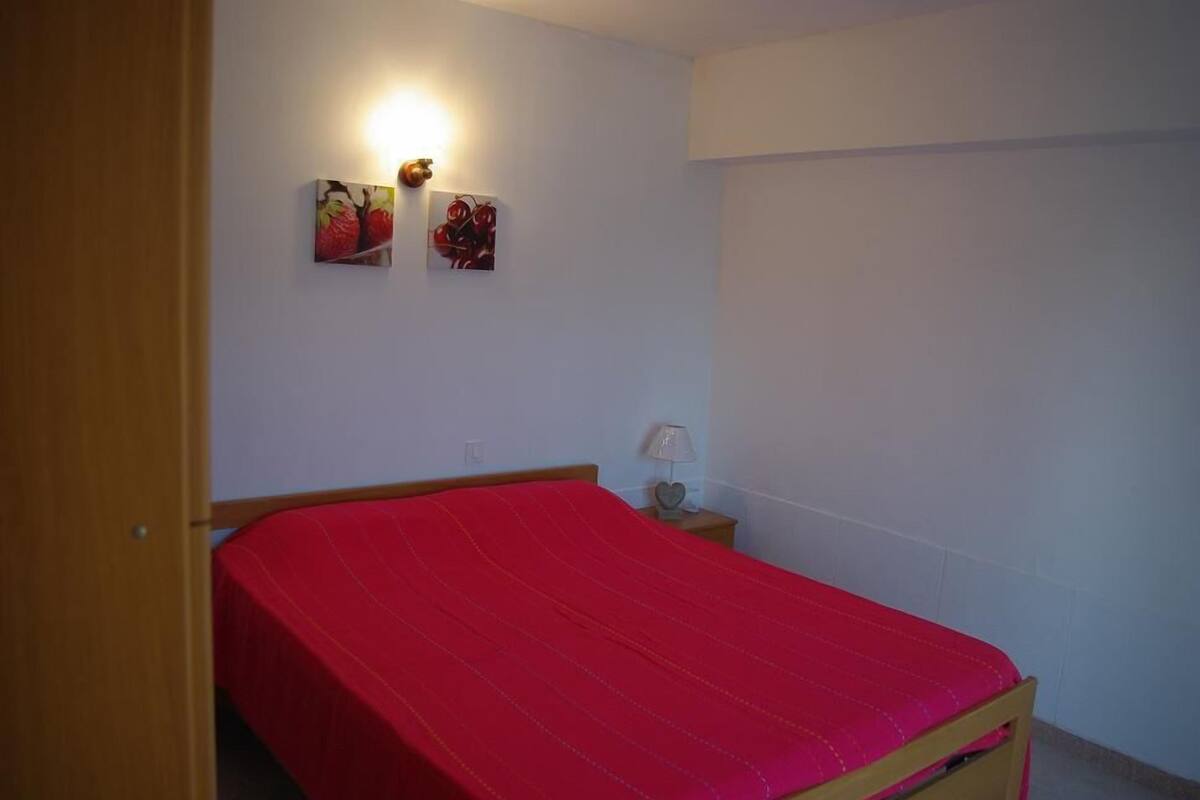 A bedroom with a single bed, a nightstand, a wall-mounted lamp, and two framed pictures.