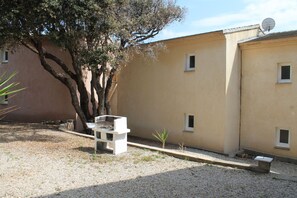 A building with a beige exterior, a tree, and a bench. - Résidence Anna (Centuri)