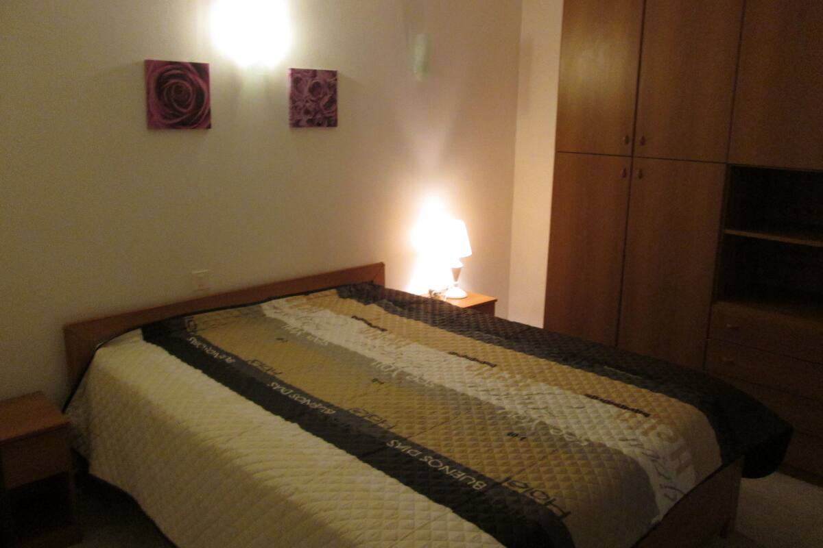 A bedroom with a bed, a nightstand, a lamp, and a wardrobe.