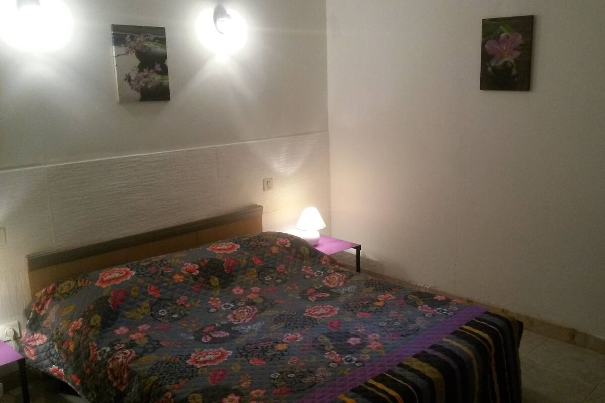 A bedroom with a floral bedspread, a bedside lamp, and two wall-mounted lights.