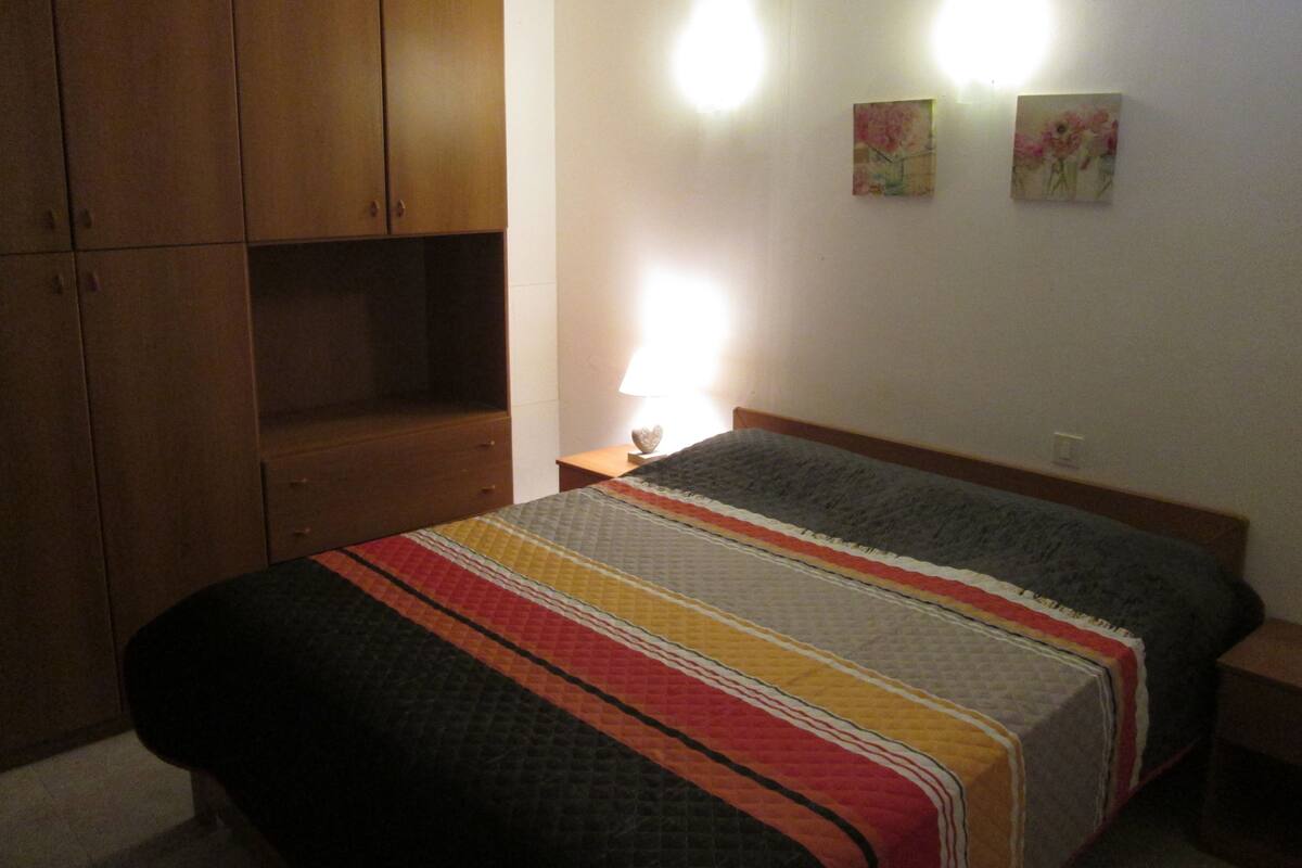 A bedroom with a bed, wooden wardrobe, and two wall-mounted lamps.