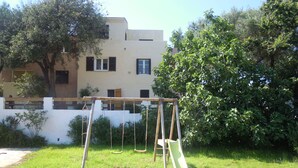 A swing set in a grassy yard with a building in the background. - Résidence Anna (Centuri)