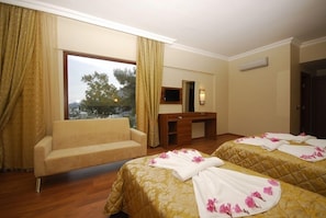 Habitación de hotel con dos camas, un sofá, un escritorio y un ventanal con cortinas.
