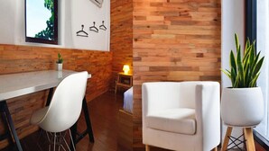 A modern room with a wooden wall, a white sofa, a dining table with chairs, and a potted plant. - The Rommanee Boutique Guesthouse (Phuket)