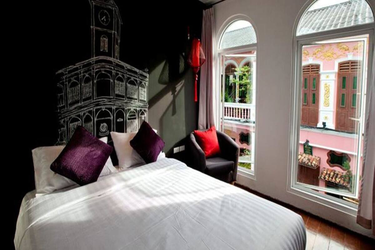 Une chambre d’hôtel avec un grand lit, une vue sur un immeuble par la fenêtre et une lanterne rouge suspendue au mur.