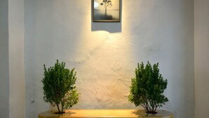 A bench with two potted plants on either side, set against a textured wall with a framed picture above. - The Rommanee Boutique Guesthouse (Phuket)