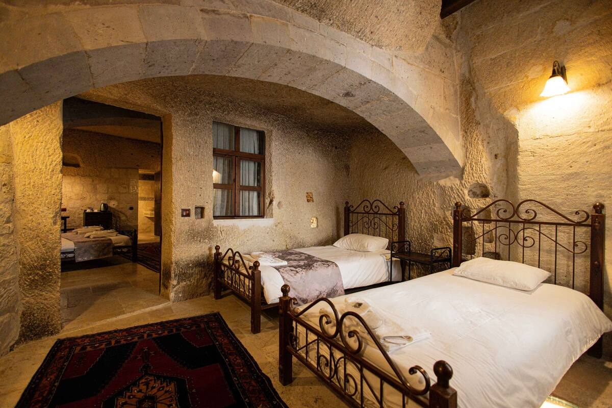 Una habitación rústica con dos camas, un arco de piedra y un ventanal pequeño.