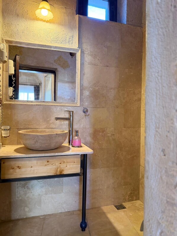 A bathroom with a large, round stone sink, a mirror above it, and a light fixture above the mirror. - Century Cave Hotel (Nevsehir)