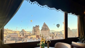 A round table with chairs in a room with a view of a cityscape and hot air balloons. - Century Cave Hotel (Nevsehir)