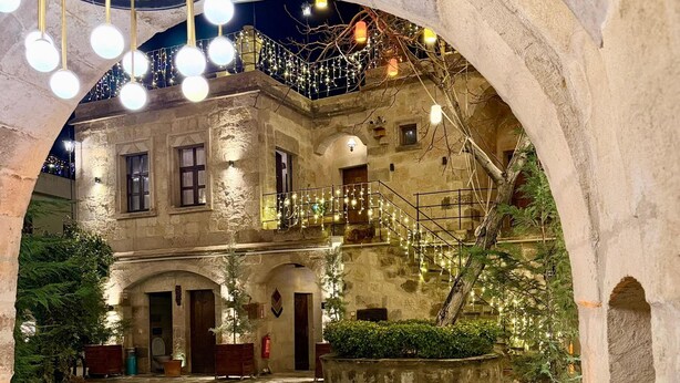 An interior courtyard with stone walls, a wooden table, and chairs. - Century Cave Hotel (Nevsehir)