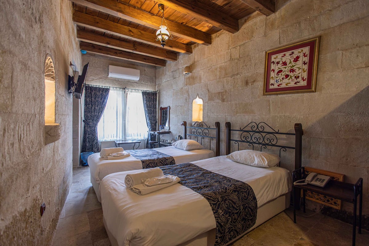 Una habitación con dos camas, techo de madera, pared de piedra, una obra de arte enmarcada y un teléfono sobre una mesita de noche.