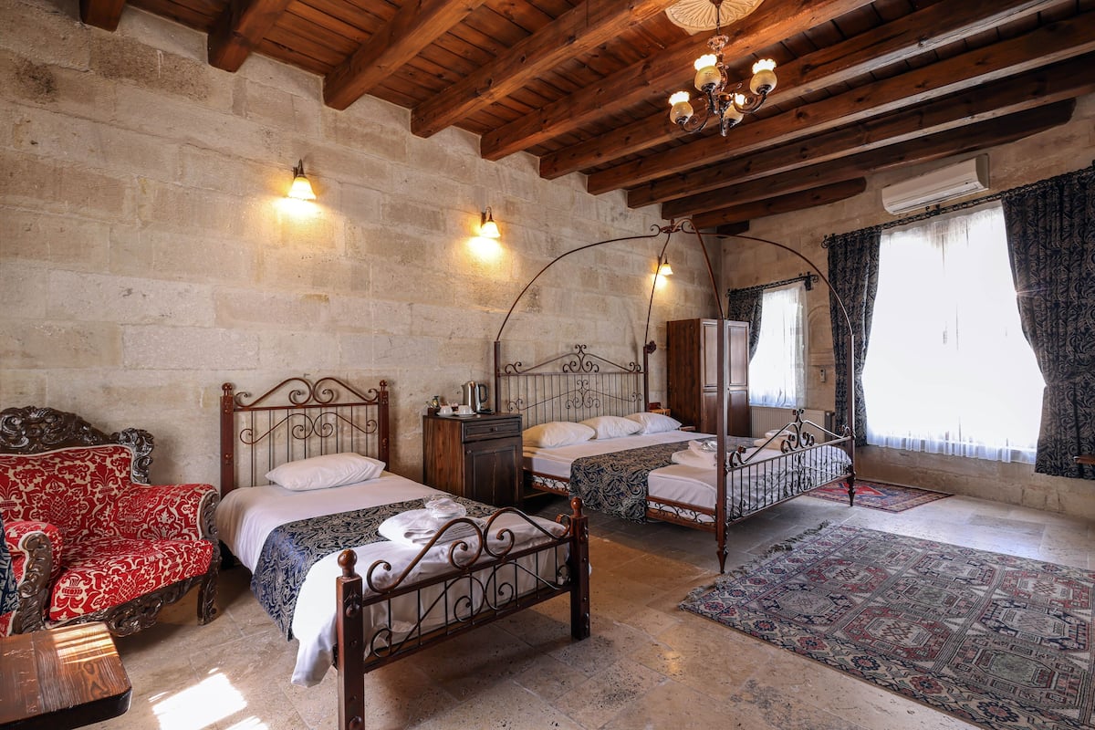 Un dormitorio con tres camas de madera, una pared de piedra y una araña.