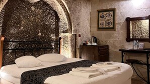 A bedroom with a stone wall, a bed, a desk, and a mirror. - Century Cave Hotel (Nevsehir)