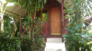 Un edificio de madera con puerta y un pequeño porche rodeado de abundante vegetación.
