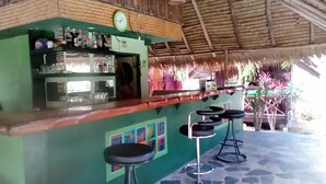 Una zona de bar con una pared verde, un reloj y un techo de paja.