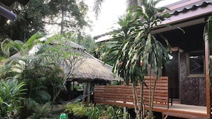 Un jardín tropical con un banco de madera, una estructura de techo de paja y diversas plantas.