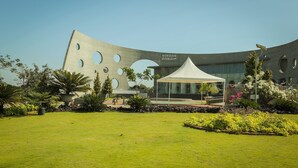 A modern building with a unique curved facade and circular cutouts, a well-maintained lawn, and a white tent in the foreground. - UVA Meridian bay resort and spa (Kundapur)