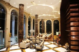 A spacious lobby with marble columns, a chandelier, and a seating area with sofas and chairs.