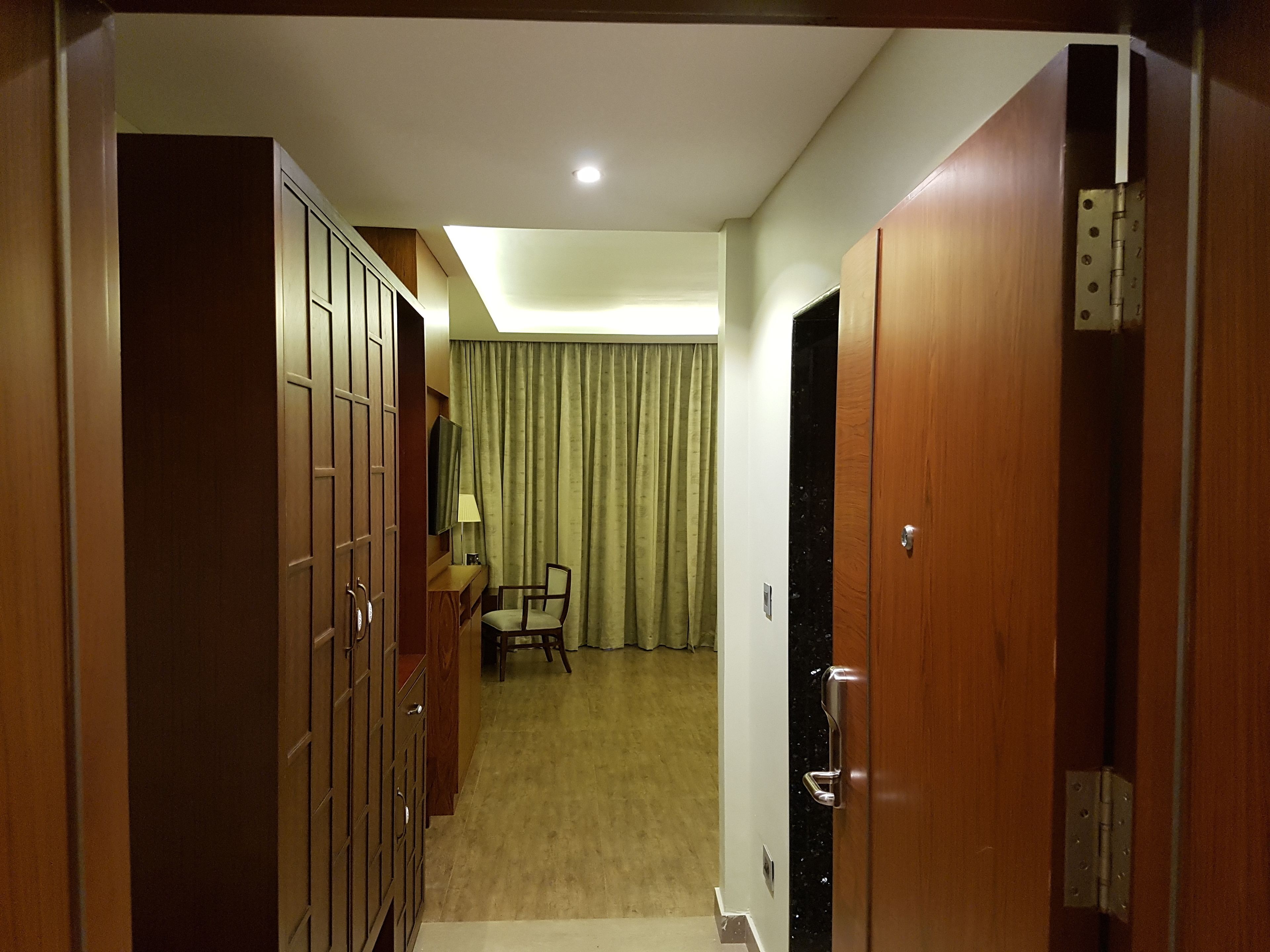 Une chambre d’hôtel avec une armoire en bois, un bureau avec une chaise, un lit et un rideau.